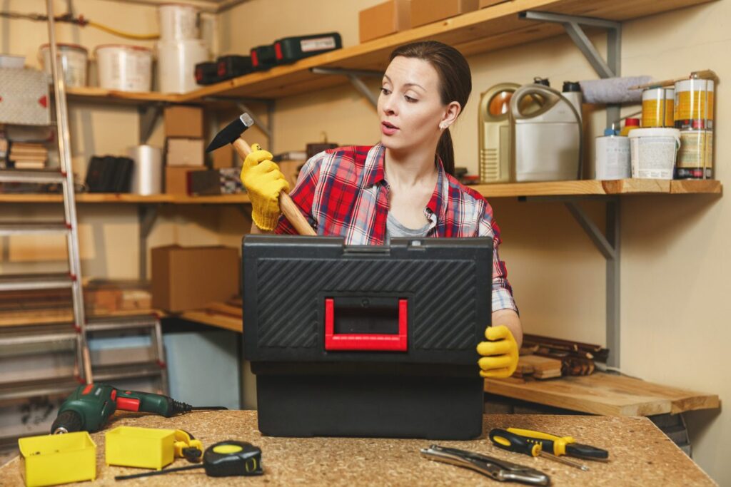 Beautiful young woman , yellow gloves working in workshop at wooden table place, took hammer out of black toolbox