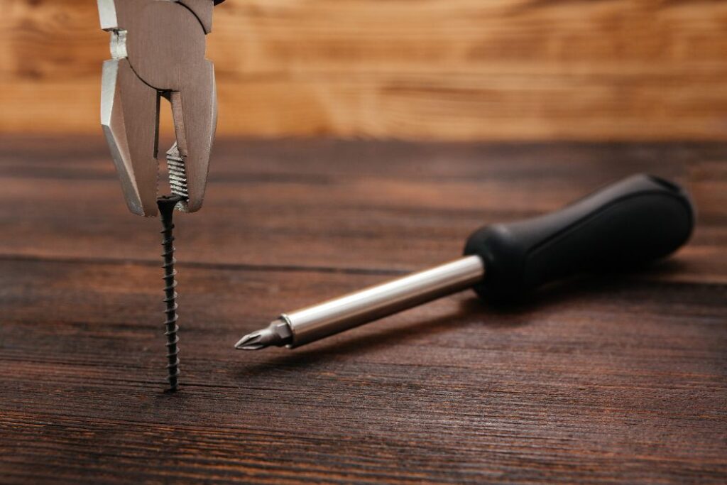 Pliers pulls out a self-tapping screw from a dark wood